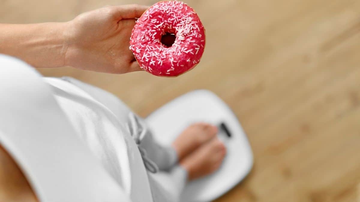 a woman holding a donut while standing on a scale.