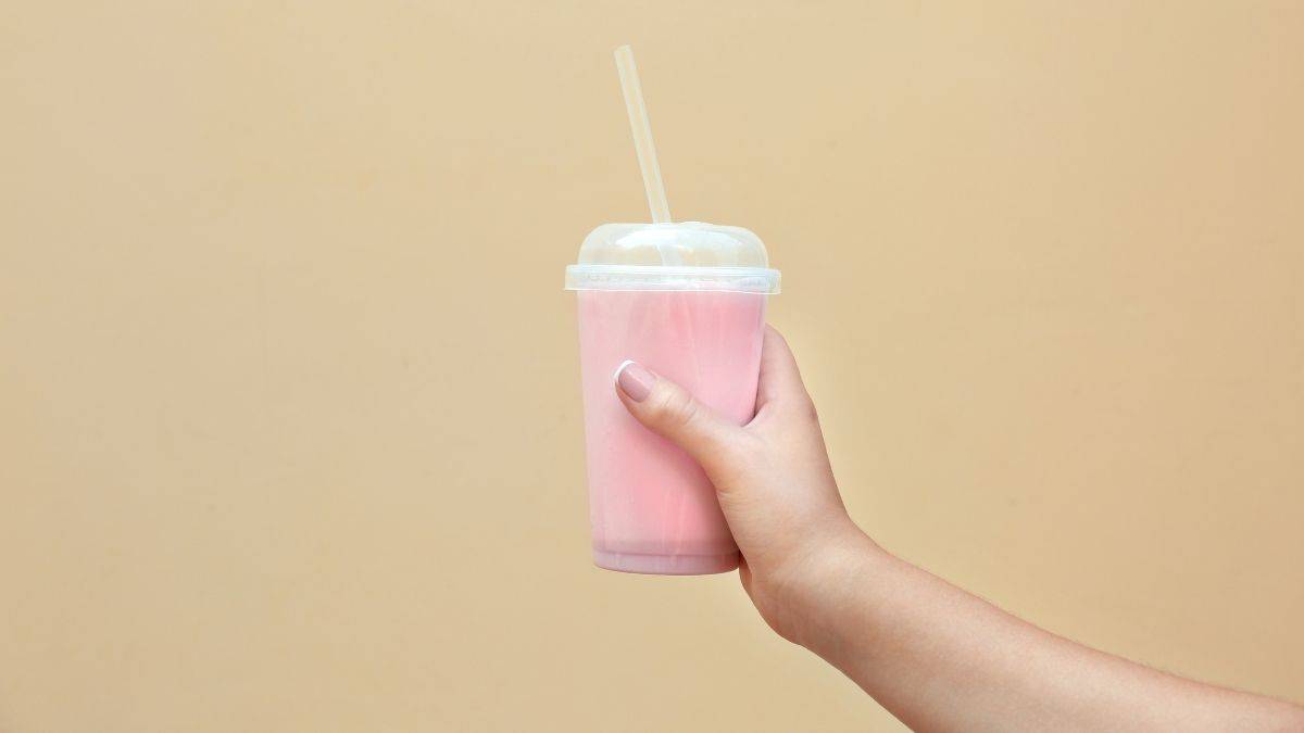 A person holding a pink meal replacement shake in a clear cup with a straw.
