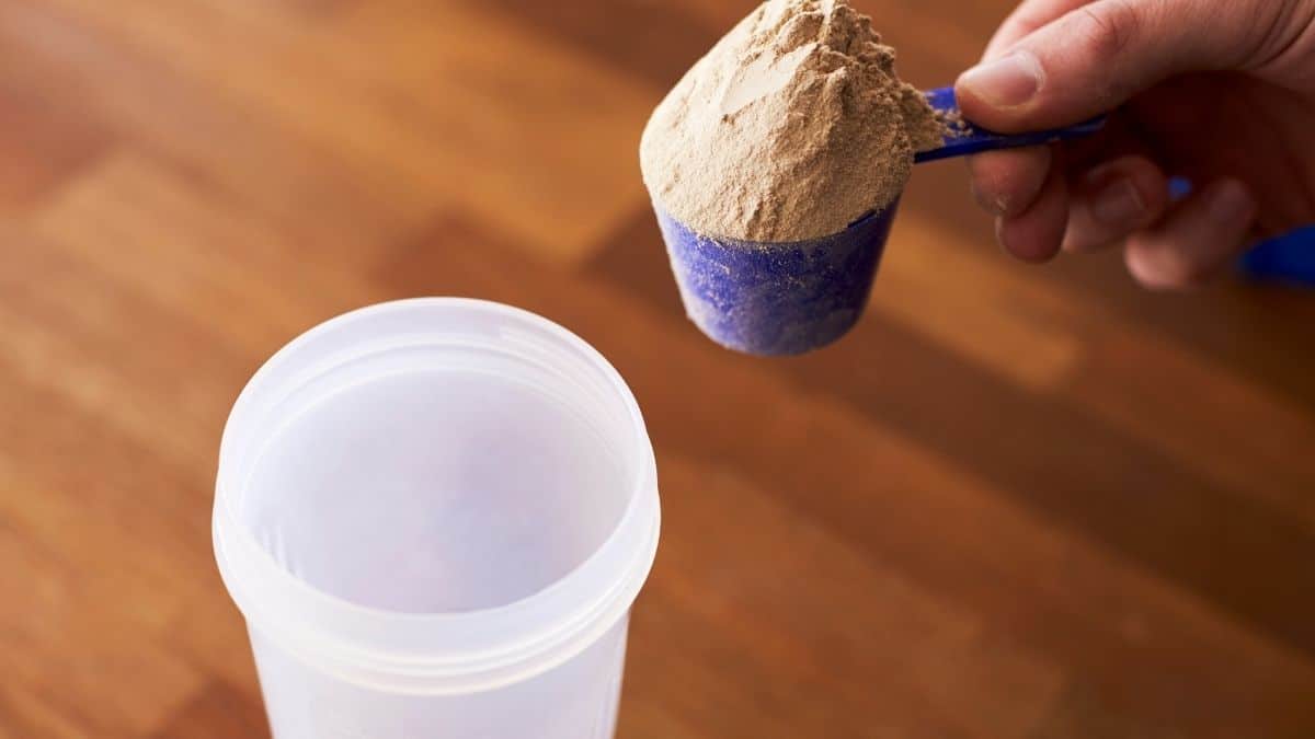 A pink scoop of powder being mixed into a protein meal replacement shake cup.