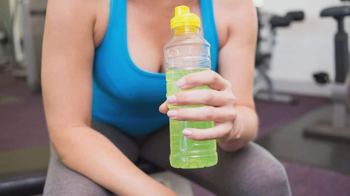 A woman in a blue tank top holding a waterbottle filled with a keto energy drink.