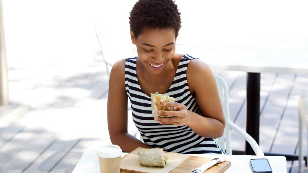 A woman smiling outside enjoying a meal.