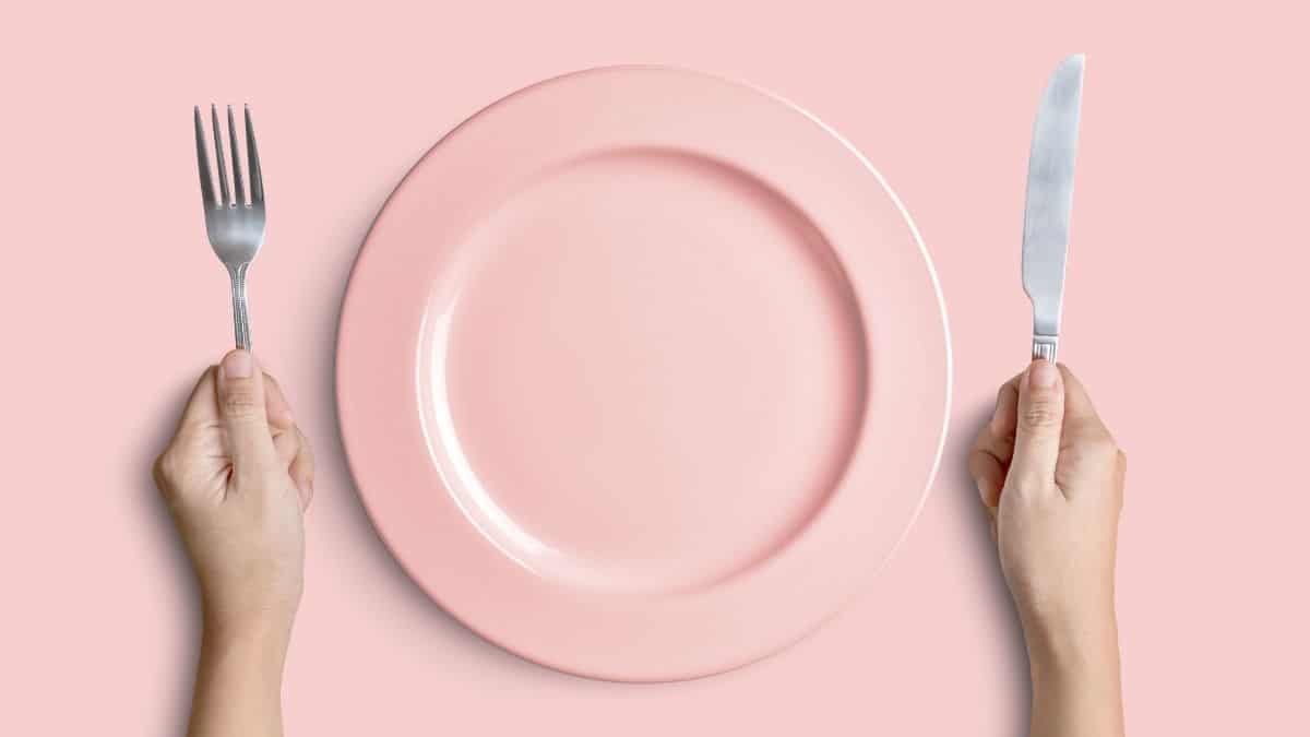 An empty pink plate with hands holding a fork and knife.