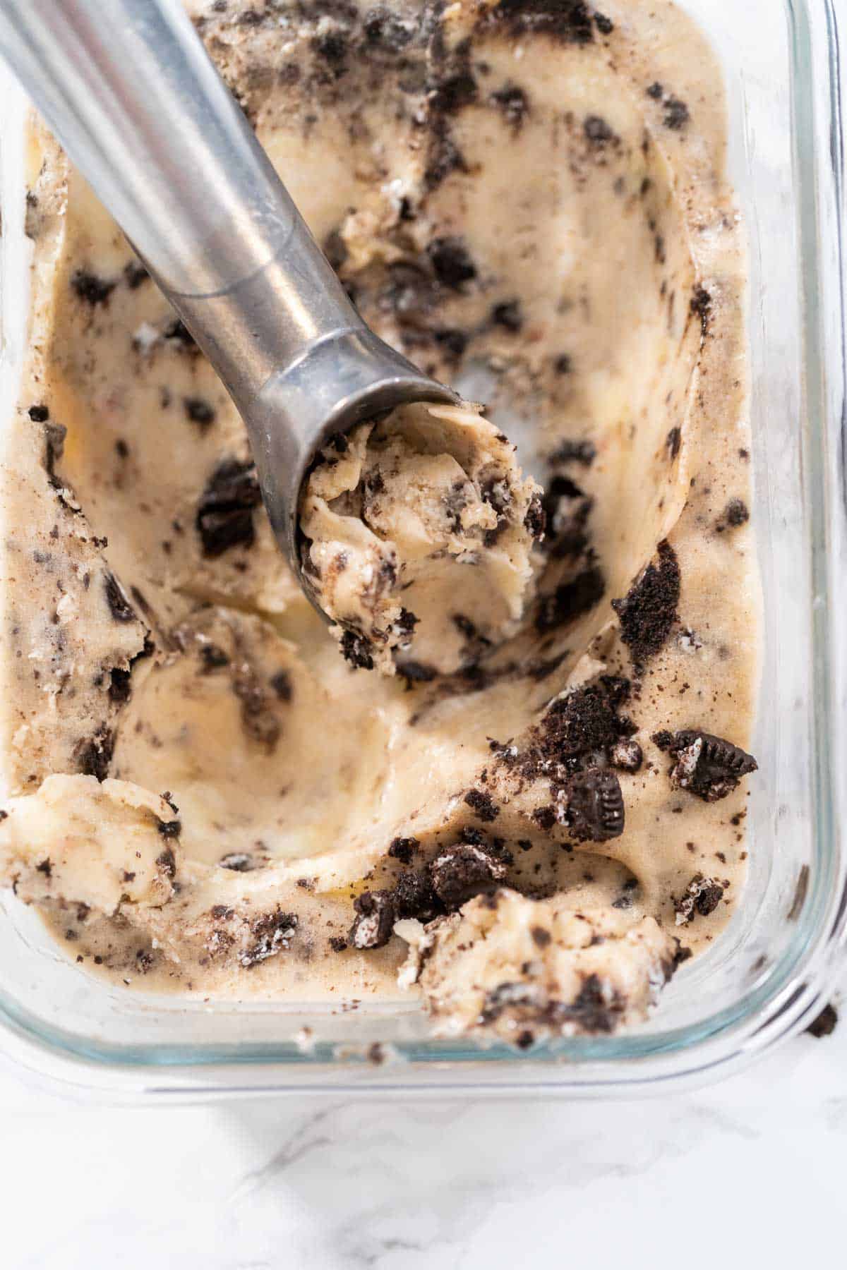 A close up image of Cookies and Cream Nice Cream in a glass container with a metal ice cream scoop.