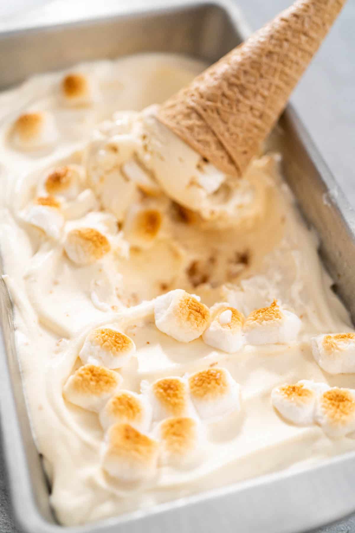 An ice cream cone in a container of no churn toasted marshmallow ice cream.