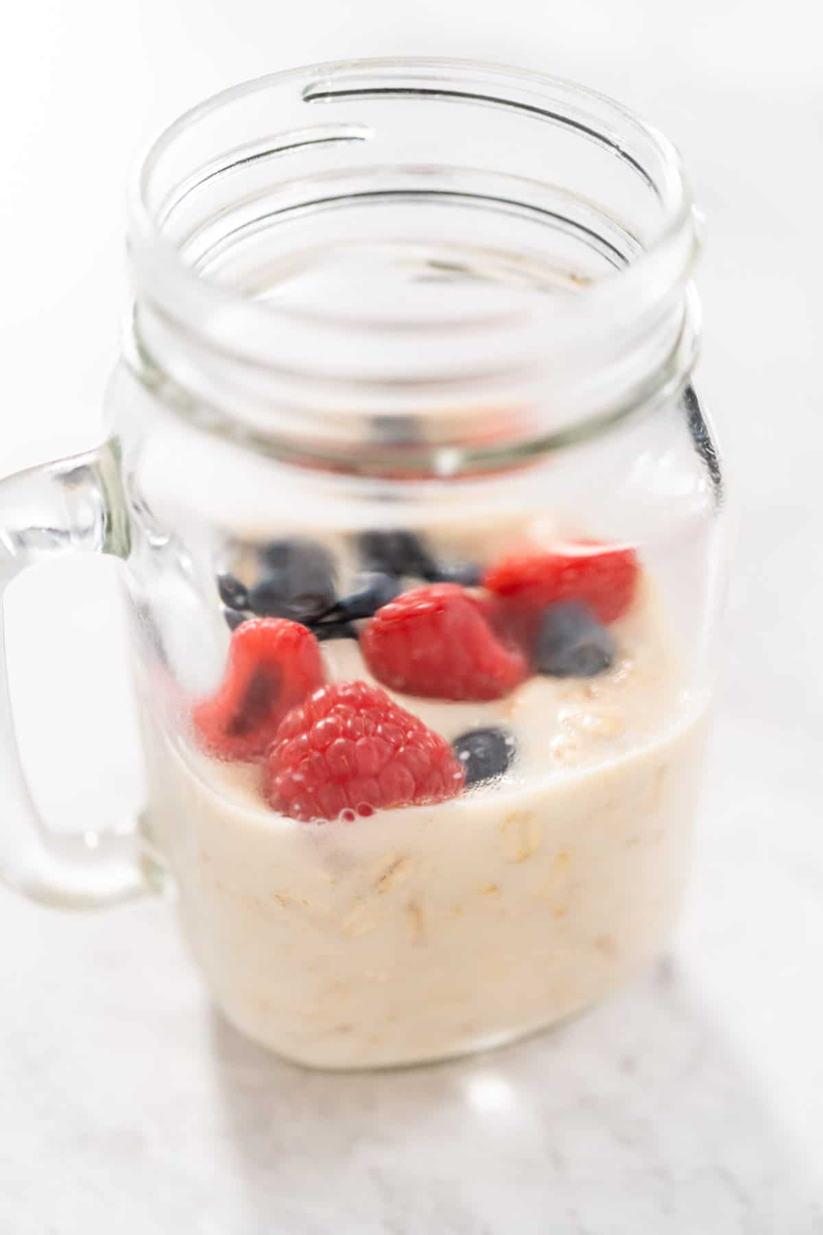 a close up shot of protein overnight oats topped with blueberries and raspberries in glass mason jar.