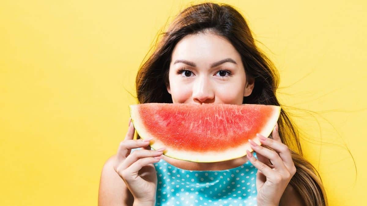 a young woman holding a watermelon slice in front of her face to look like a smile, an example of a restricted food on the slow carb diet.