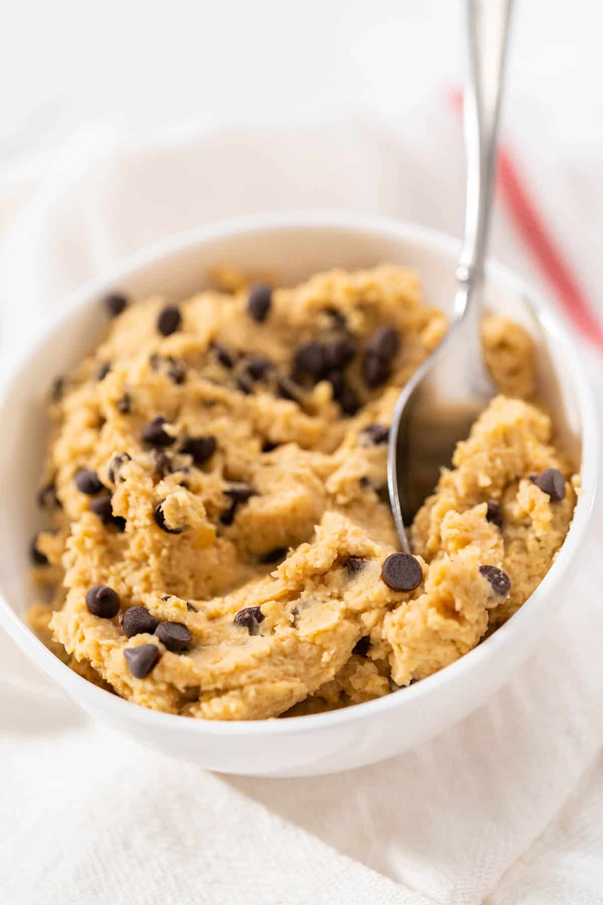 close up of Chocolate Chip Cookie Dough Hummus in a white bowl with a metal spoon.