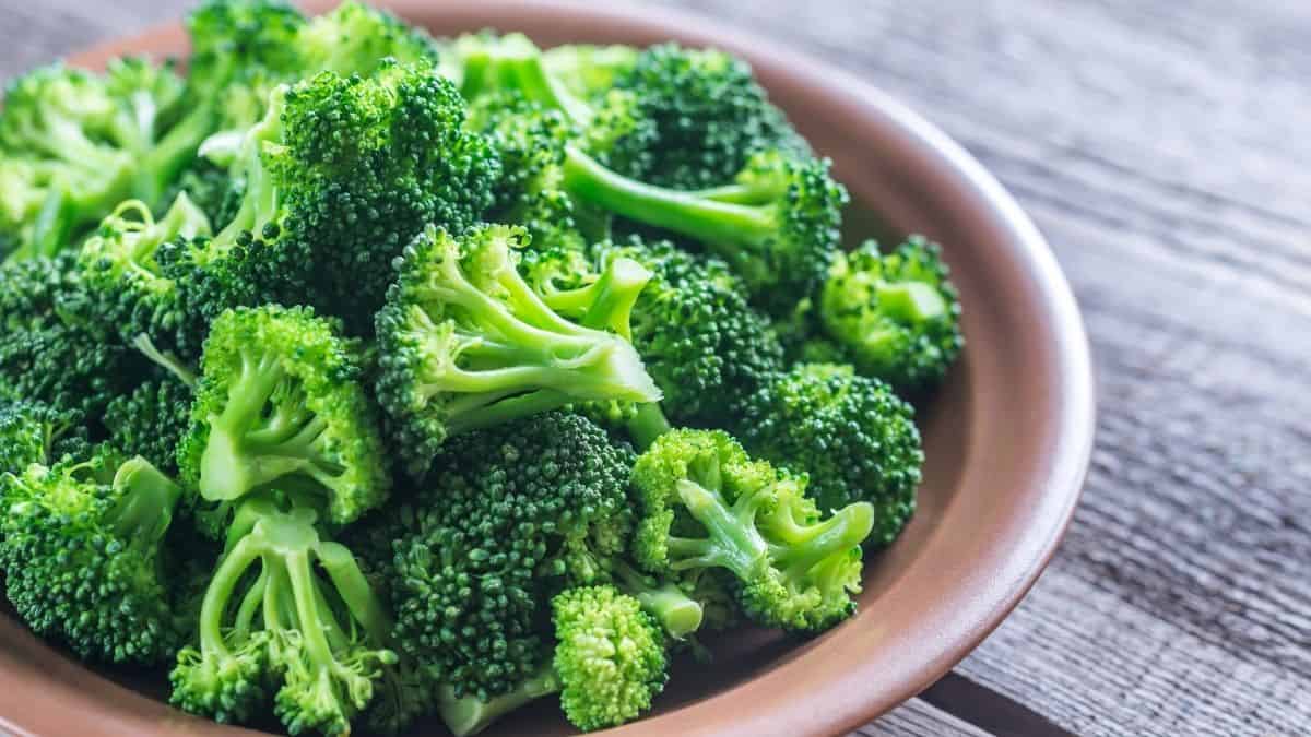vibrant steamed broccoli in a brown bowl resting on a wood table, an example of a food allowed on the slow carb diet.