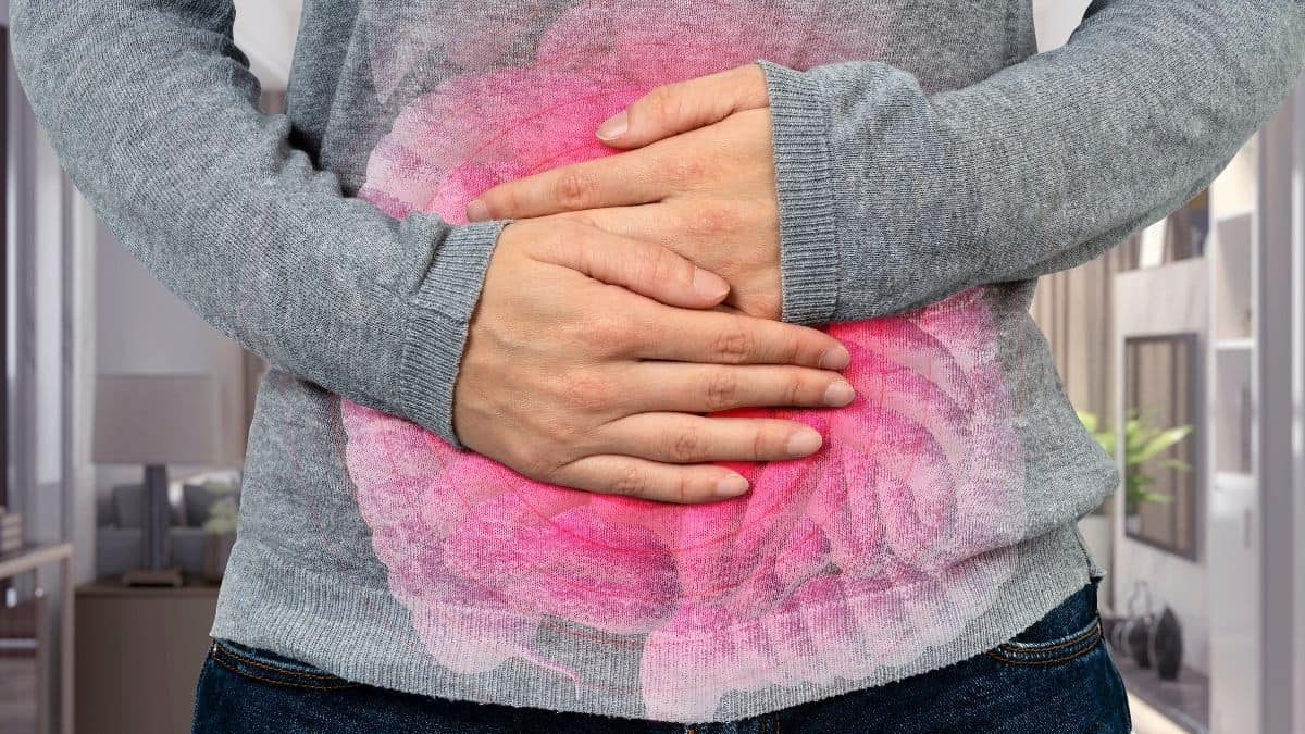 woman wearing grey sweater holding stomach to signify constipation.