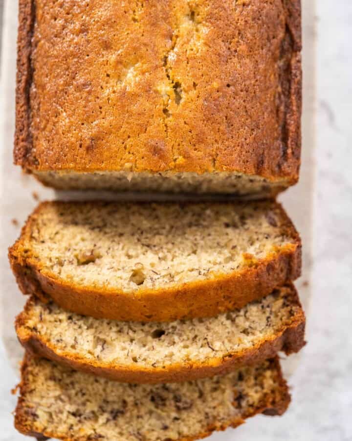 A loaf of banana bread with the first three slices leaning onto counter for one bowl banana bread.