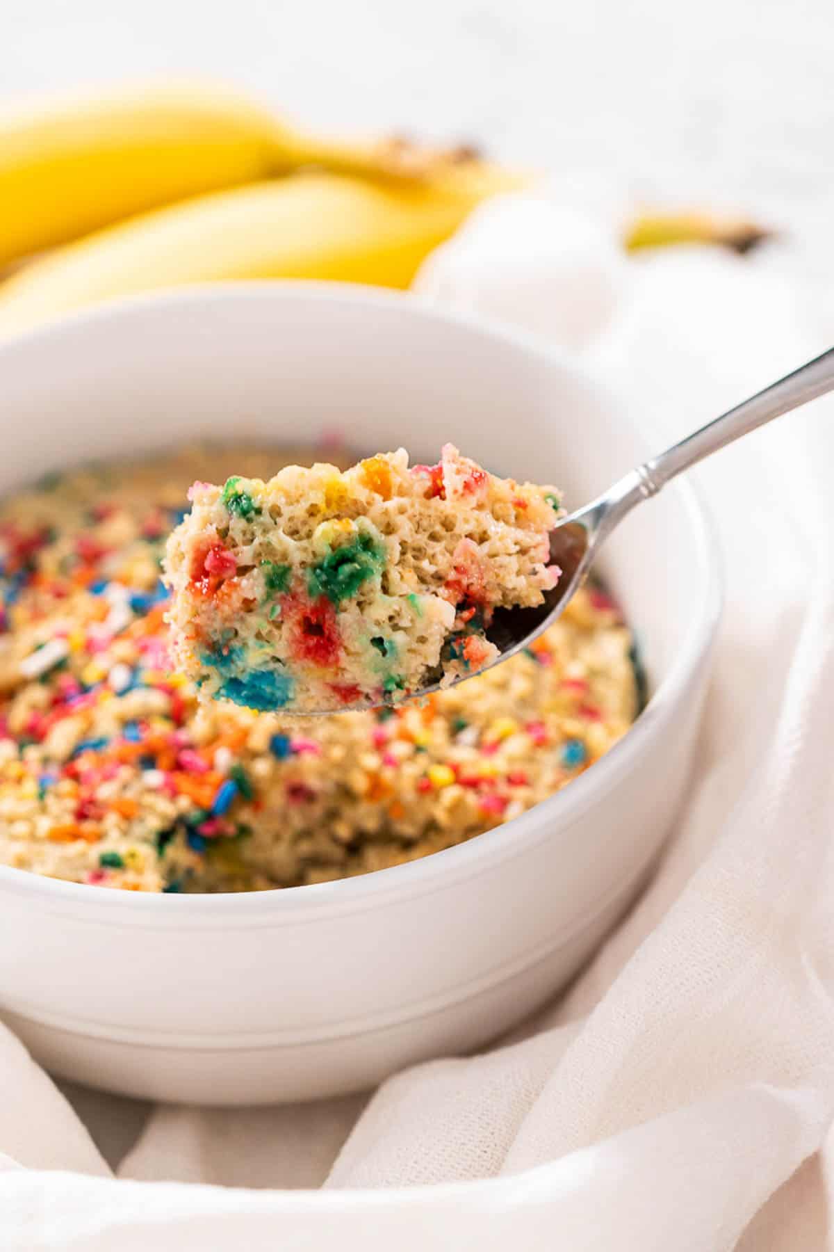 A white bowl of Baked Birthday Cake Oatmeal with a close up of a spoonful to show texture.