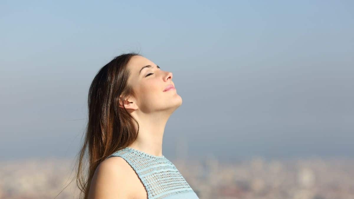 A woman with her eyes closed taking a deep cleaning breath, a way to help lower cortisol levels and anxiety.