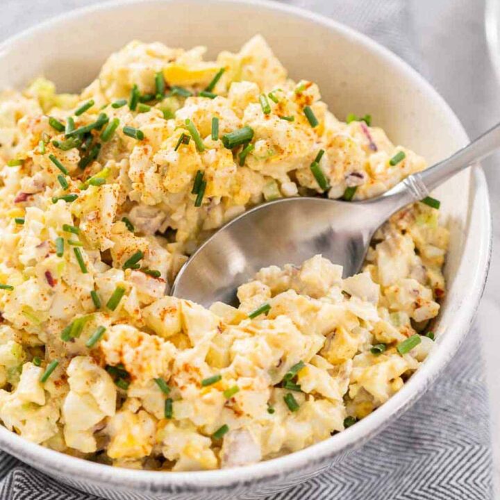 Instant Pot Egg Salad in a bowl with a metal spoon taking out a scoop in a white bowl.