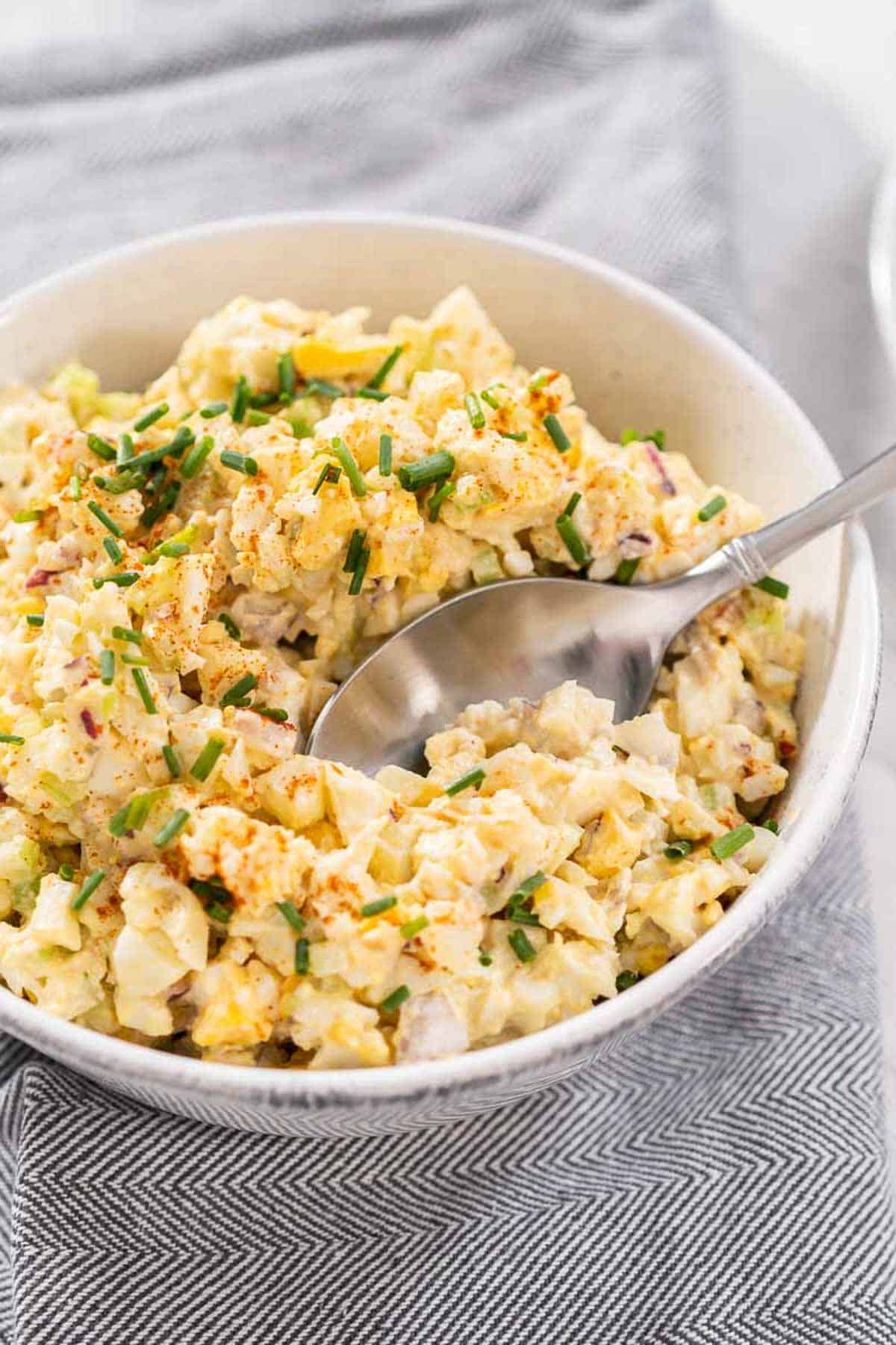 Instant Pot Egg Salad in a bowl with a metal spoon taking out a scoop in a white bowl.