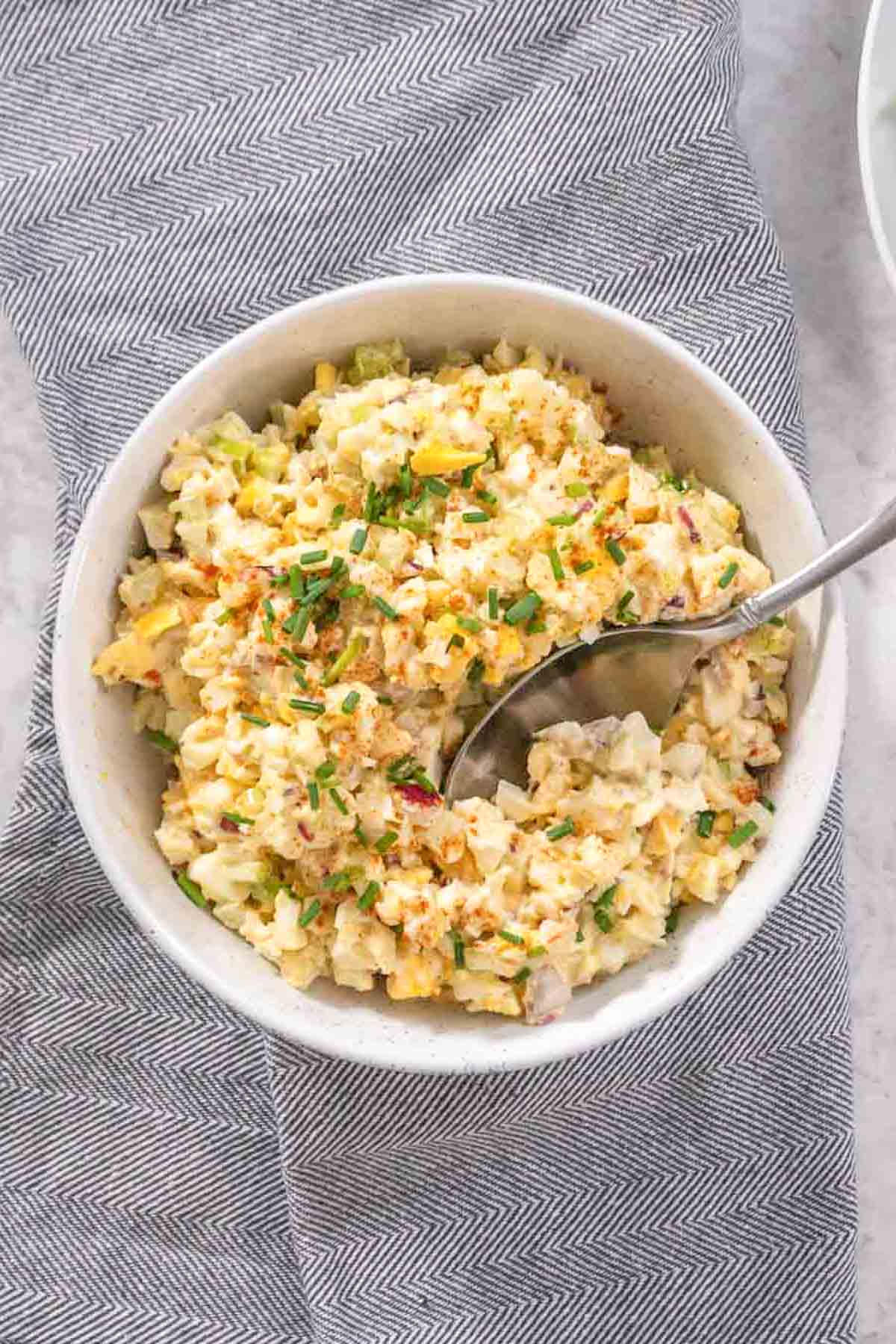Top down view of Instant Pot Egg Salad in a white bowl with a metal spoon scooping out a bite.