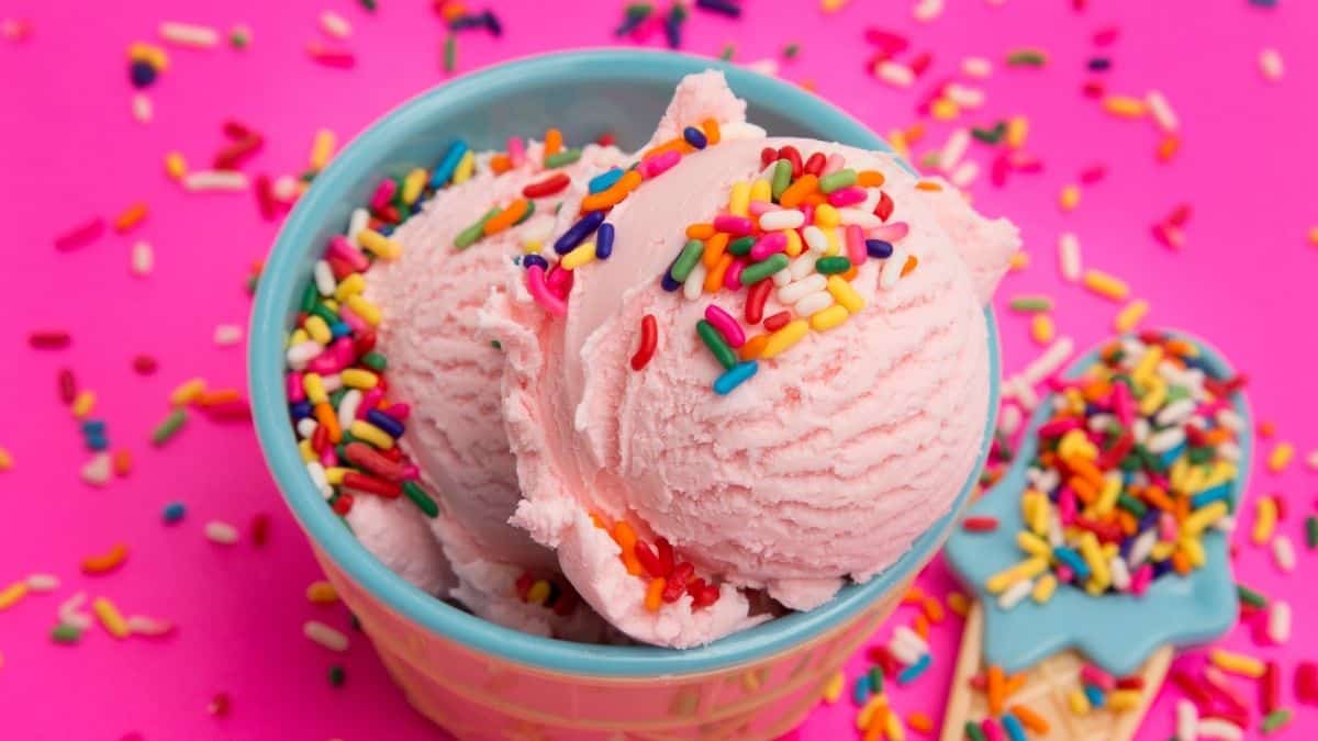 a dish of two scoops of strawberry ice cream in a tan and blue bowl covered in sprinkles on a pink background, which could be an example of emotional eating.