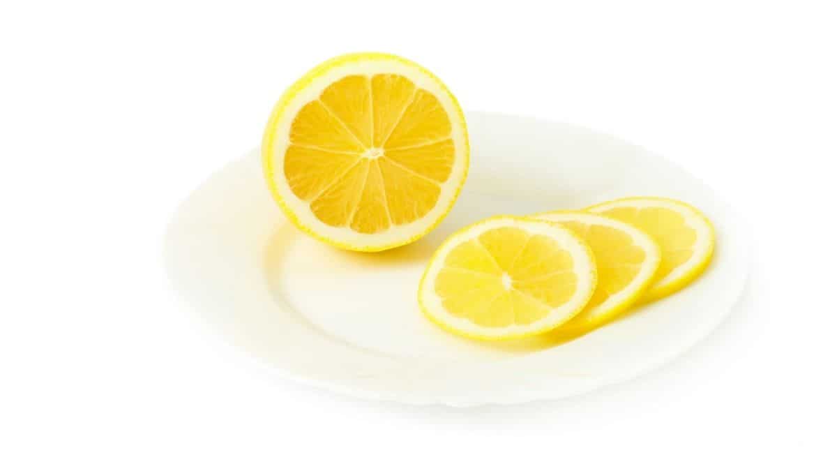 a lemon on a white plate, half of it sliced.