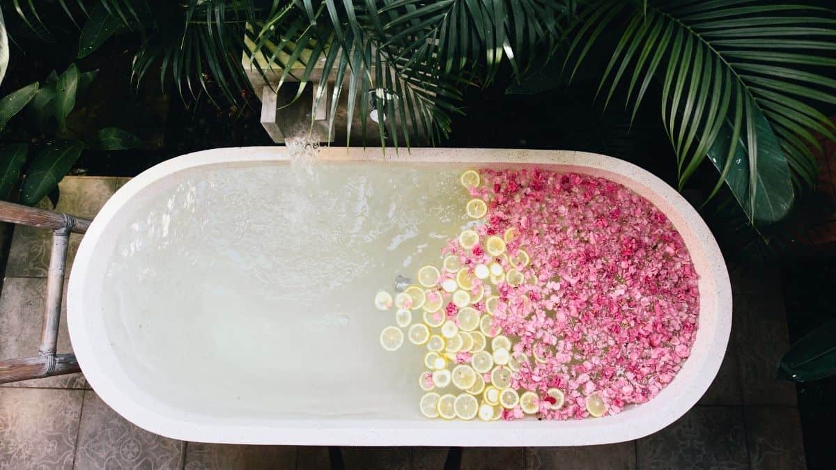 a-white-oval-bathub-filled-with-pink-flower-petals-and-lemon-slices-ready-for-an-emotional-self-care-bath.