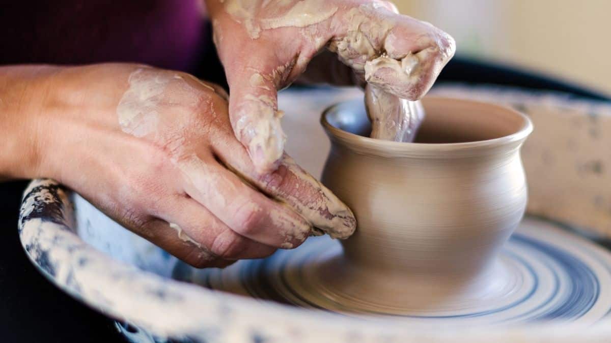 a woman at a potters wheel throwing a clay pot; we see her hands shaping the pot, this is an example of emotional self care.