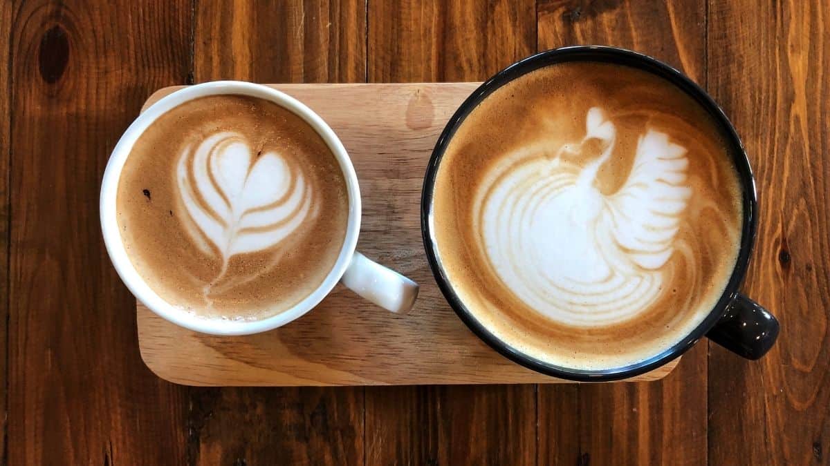 two cups of coffee with latte art, one is larger in a black mug and the other smaller in a white mug, an example of emotional self care.