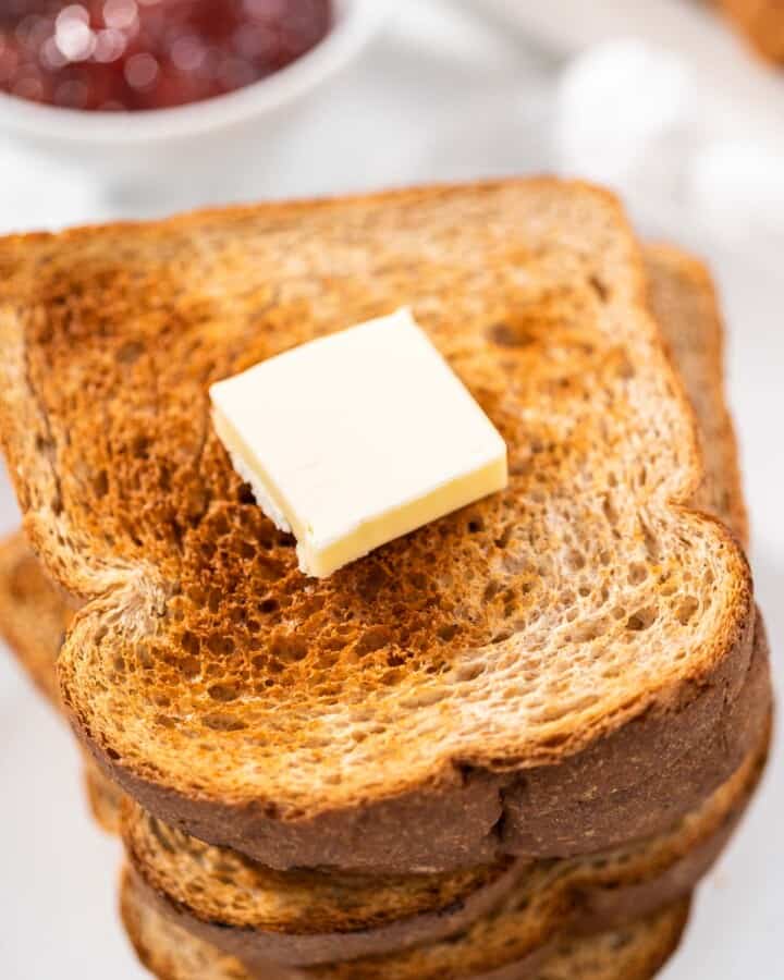 A close up of a stack of air fryer toasts with a pat of butter on top and jam in the background.