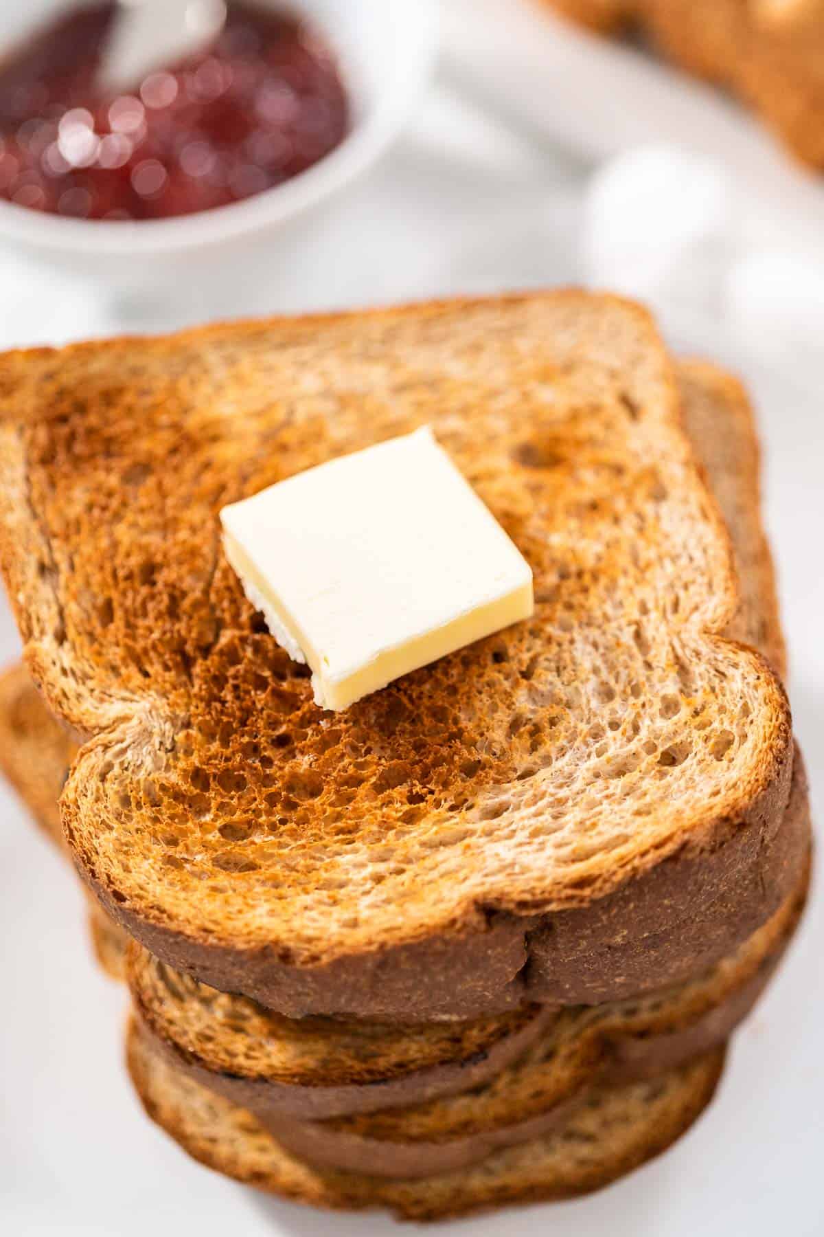 A close up of a stack of air fryer toasts with a pat of butter on top and jam in the background.