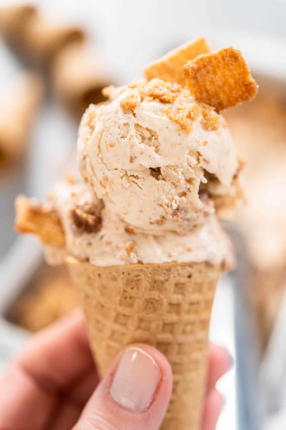 A close up of a woman holding a No Churn Cinnamon Toast Crunch Ice Cream on a waffle cone.