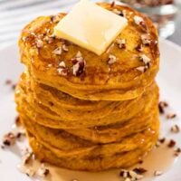 A picture of Bisquick Pumpkin Pancakes with butter, pecans and maple syrup drizzled atop.