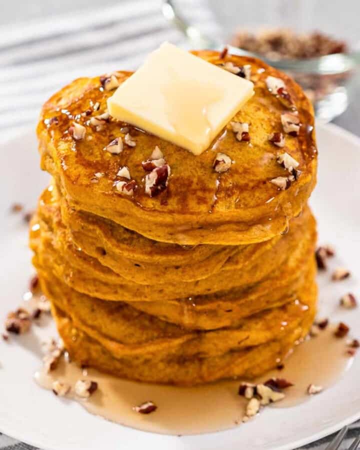 A picture of Bisquick Pumpkin Pancakes with butter, pecans and maple syrup drizzled atop.
