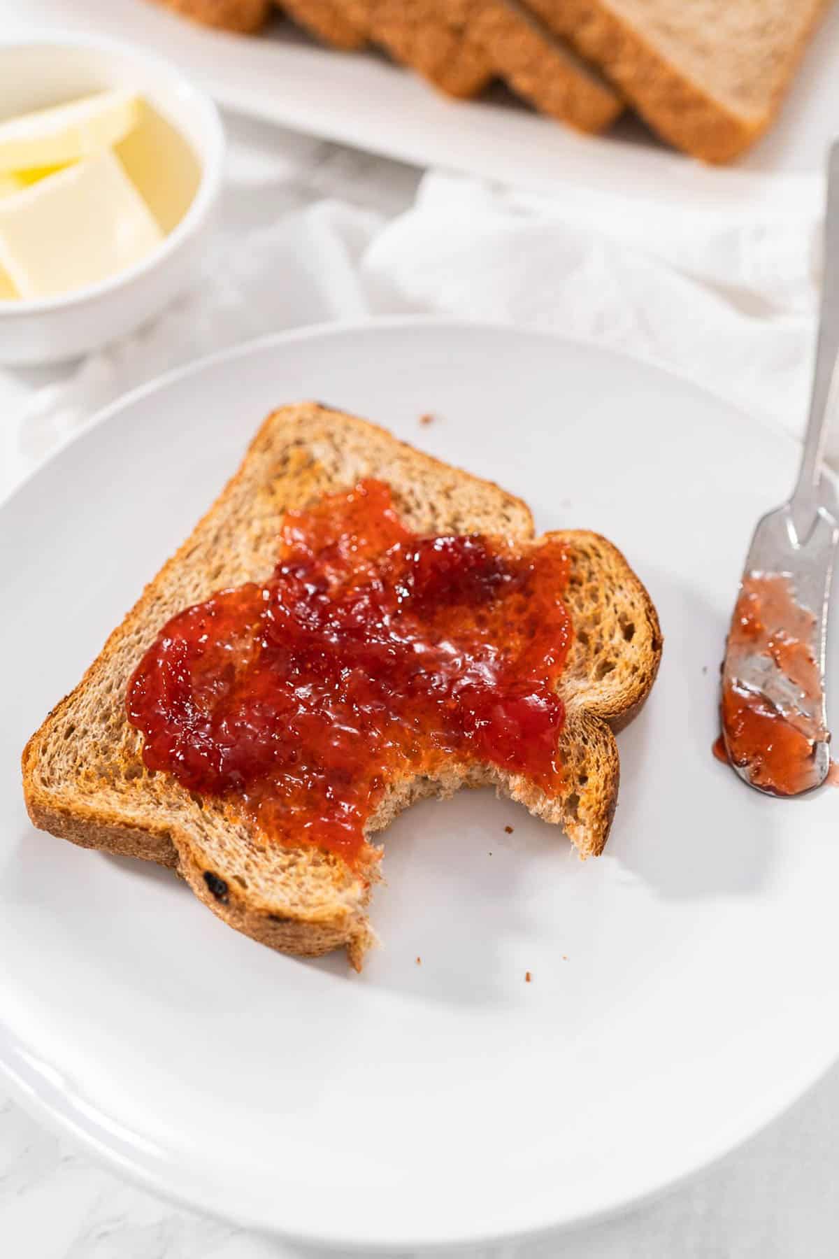 A piece of air fryer toast with strawberry jam on top with a bite taken out.