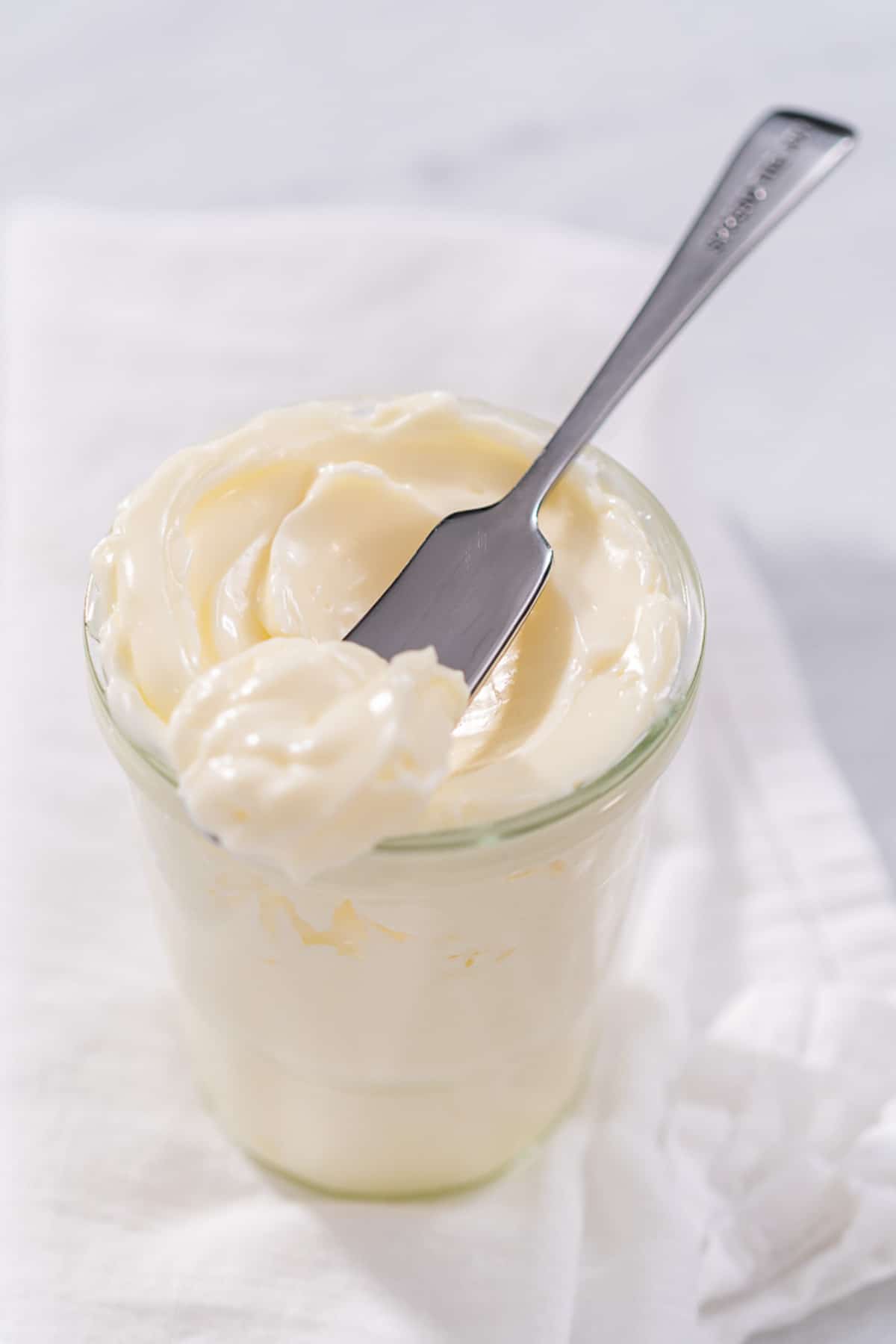 Whole Egg Mayo in a glass jar with metal knife taking a scoop out.