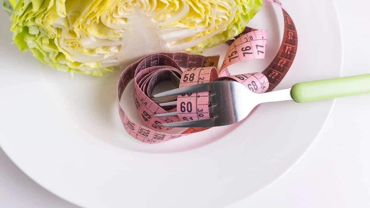 a measuring tape wrapped around a fork on a white plate, a tool a dieter may use.