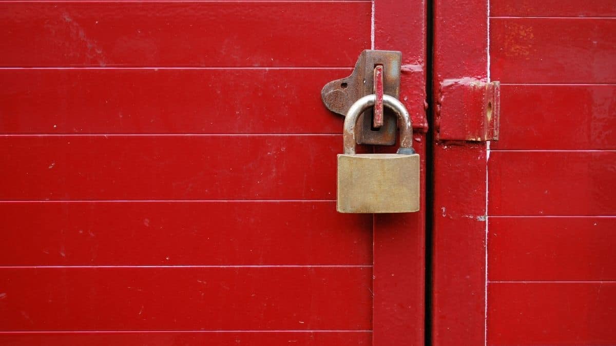 a padlock on a door latch holding a red wooden gate shut.