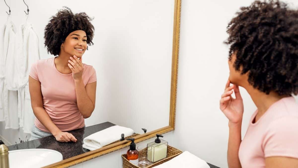a woman looking at herself in a mirror, something that could be hard for someone with a negative body image.