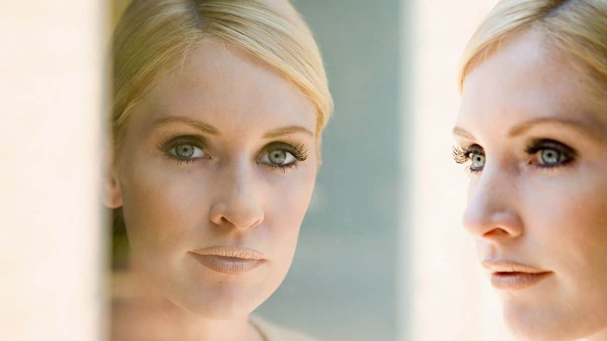 a woman with blonde hair look at her reflection in the mirror, possibly contemplating the disadvantages of dieting.