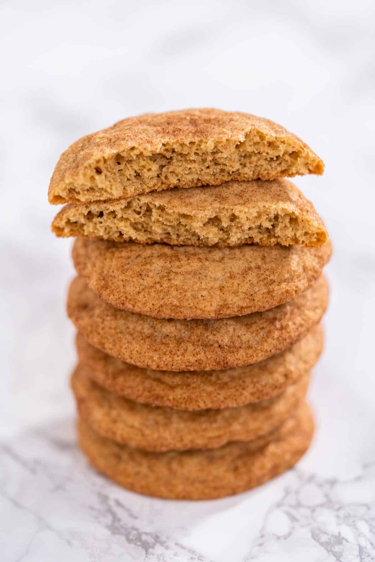 A stack of snickerdoodle cookies with the top cookie split in half to show texture.