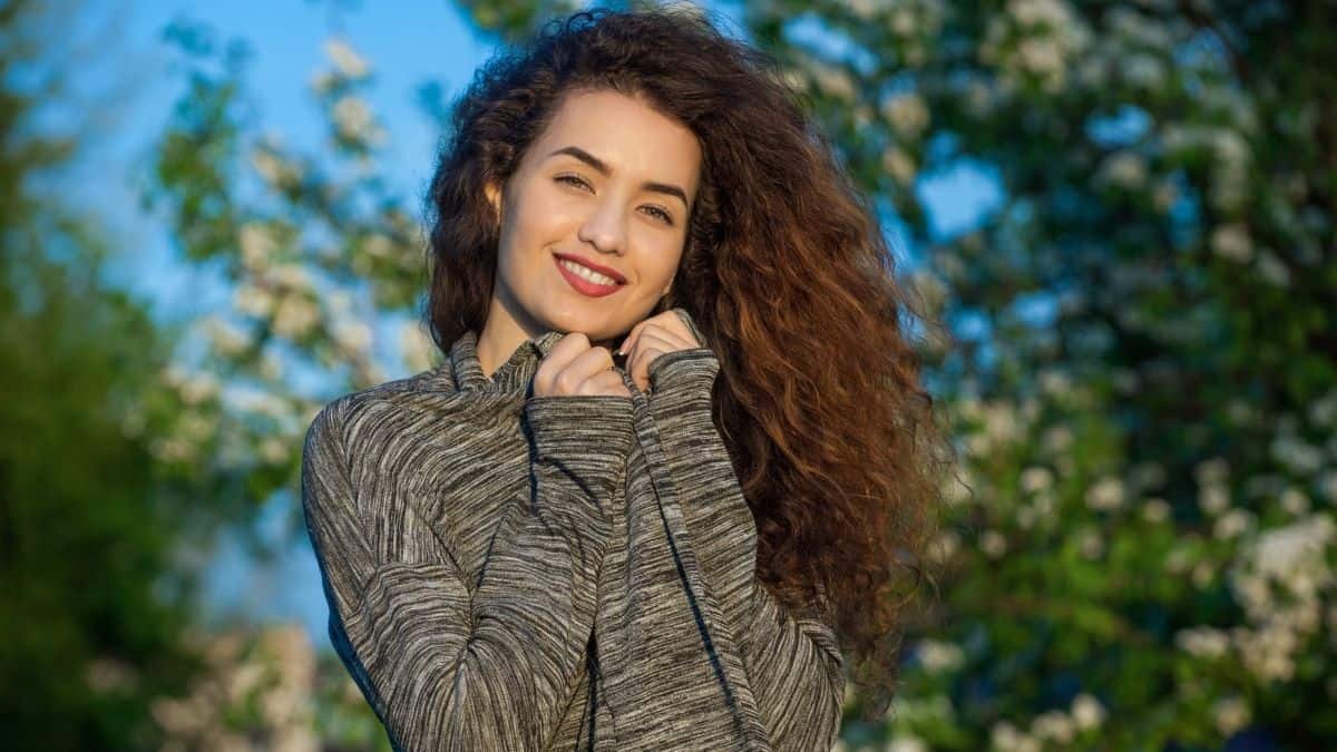 A woman in nature with a grey sweatshirt on smiling broadly.