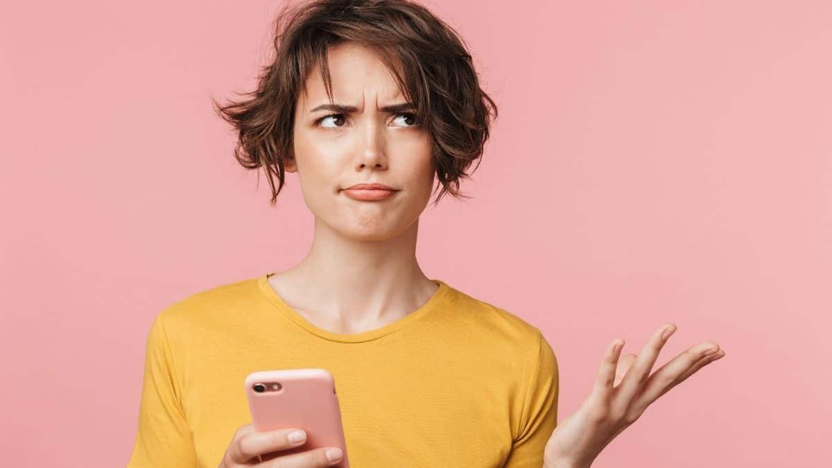 A woman looking a bit confused as she reads something on her phone.