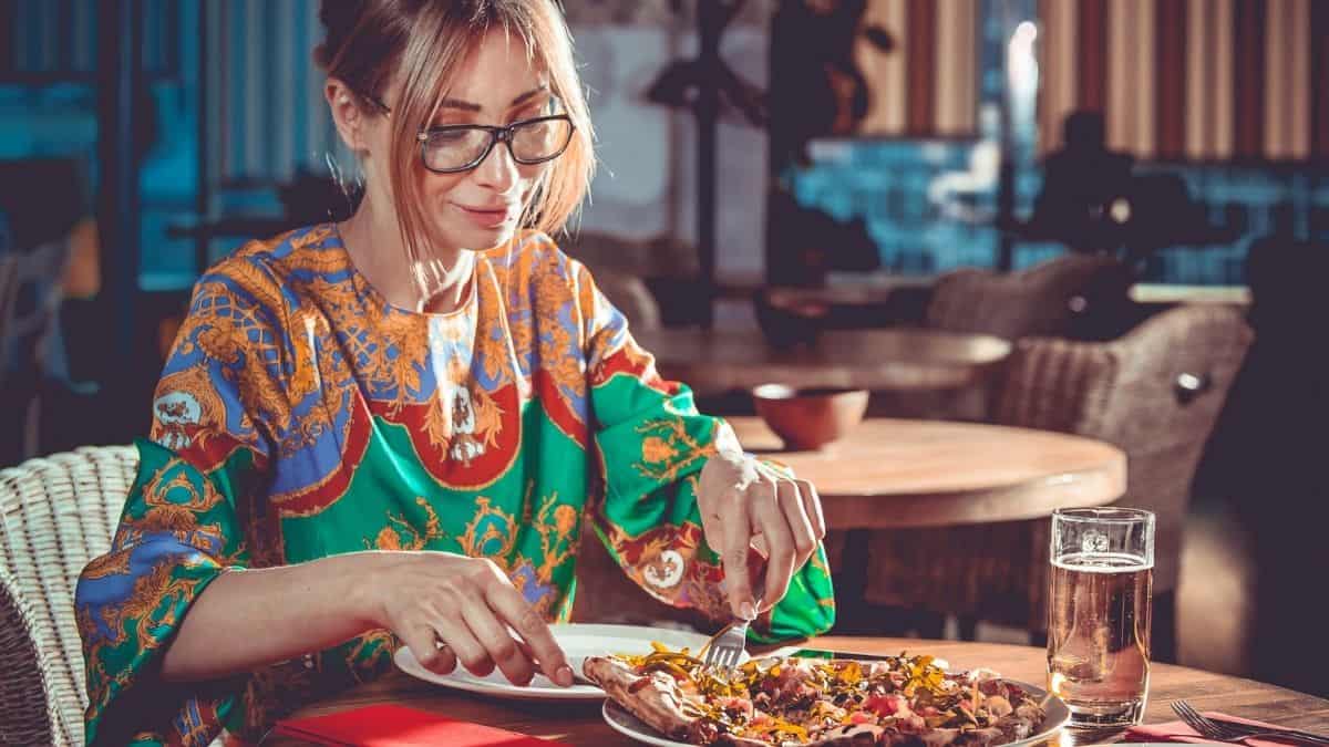 A woman peacefully enjoying a meal in a restaurant, she looks at peace with with food and her body, something an intuitive eating dietitian can help with.