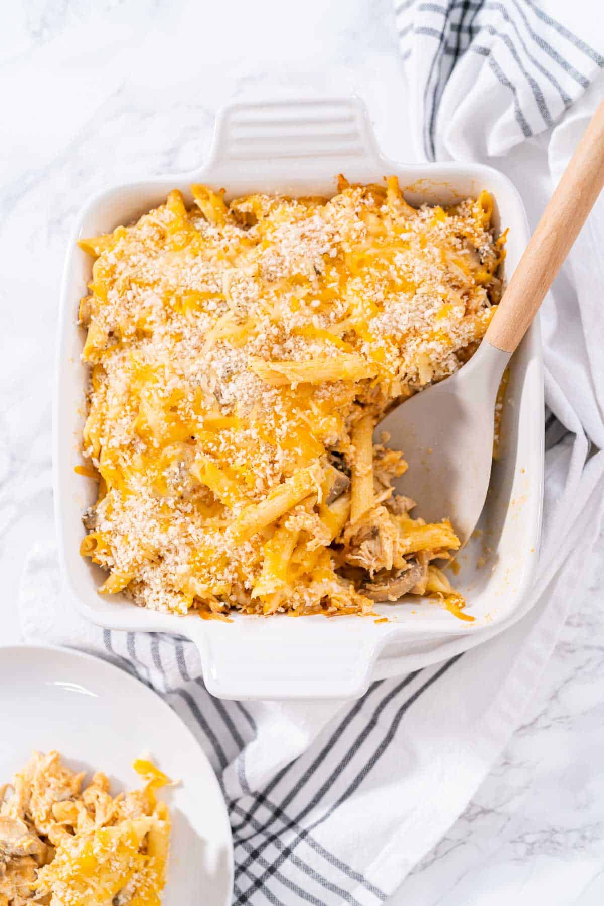 An overhead shot of Buffalo Chicken Pasta Bake with a serving on a white plate next to casserole dish.