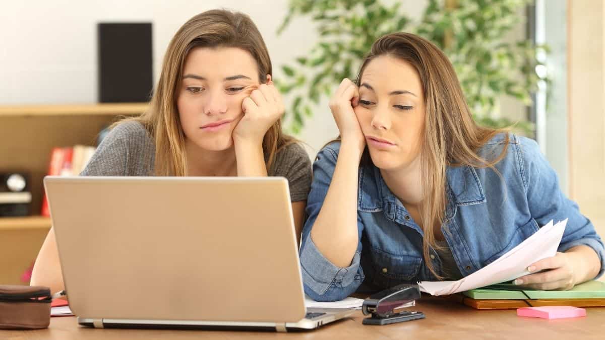 Two college-aged women looking very bored at their laptop, it may be hard to stop eating when bored for many.