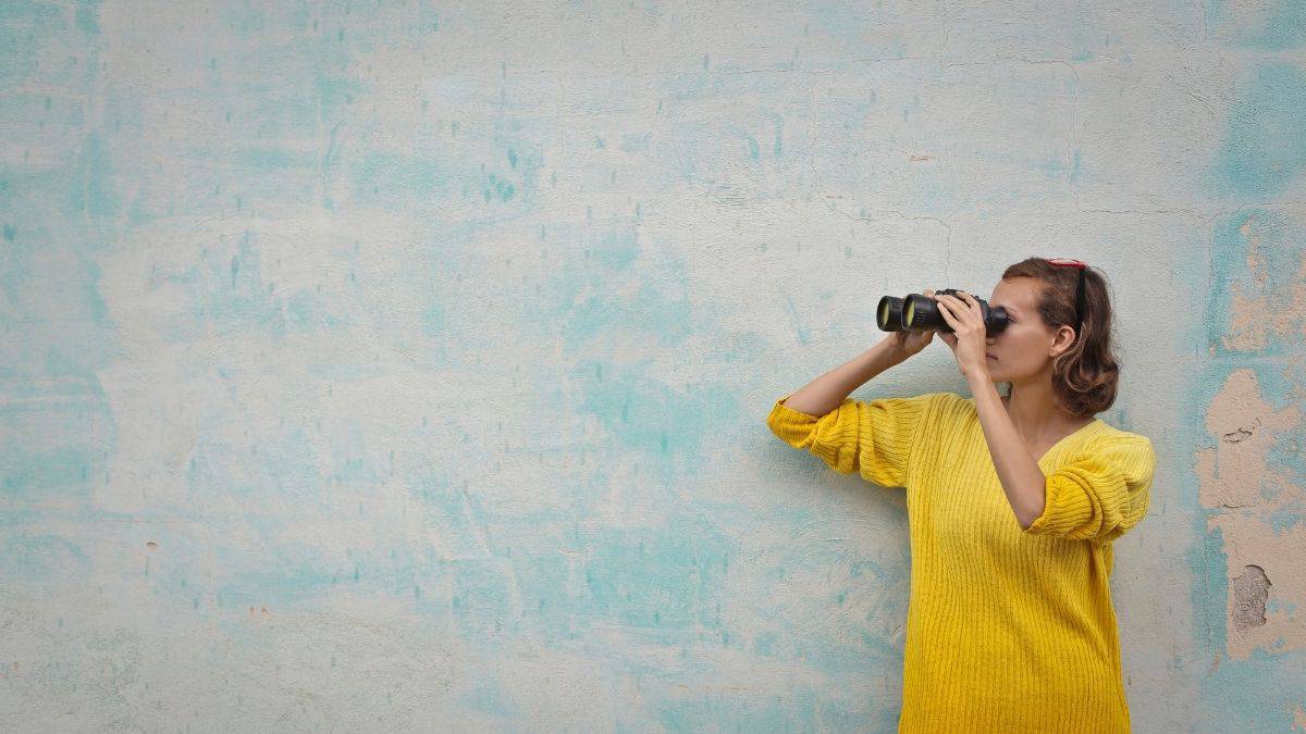 a woman in a yellow sweater looking through a pair of binoculars.