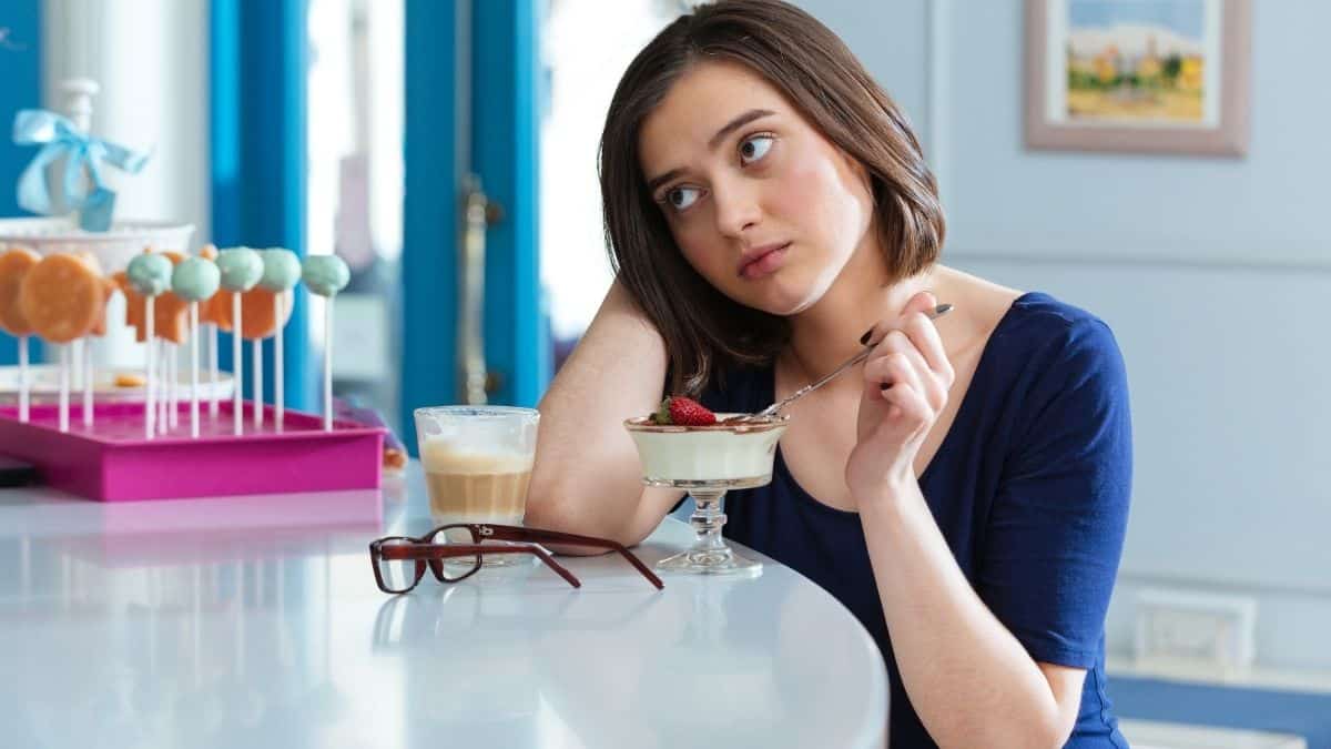 a woman slumped on the counter as she eats dessert, she has not learned to enjoy eating out.