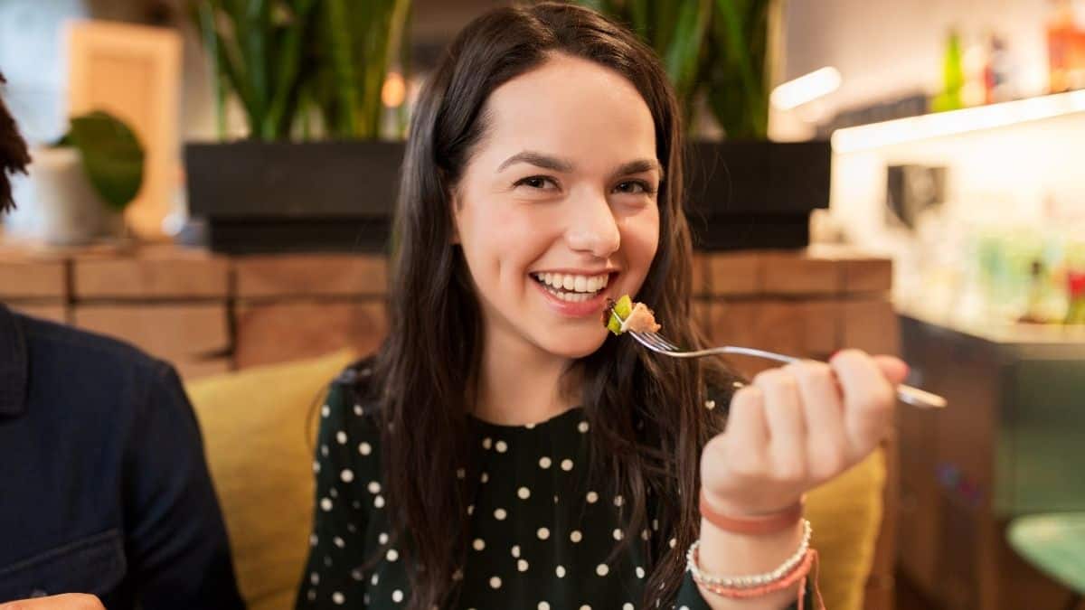 a woman taking a bite of a delicious appetizer at a fun restaurant, she has learned how to enjoy eating out.