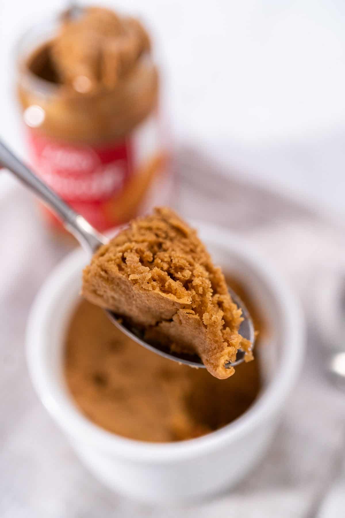A scoop of biscoff mug cake on a metal spoon hovering over the cake in a white ramekin.