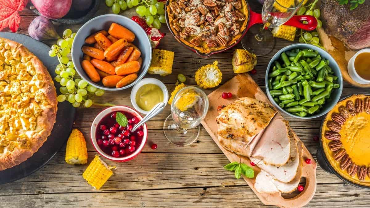 A thanksgiving feast of pie, carrots, cranberries, turkey breast and green beans on a wooden table, an example of holiday eating.