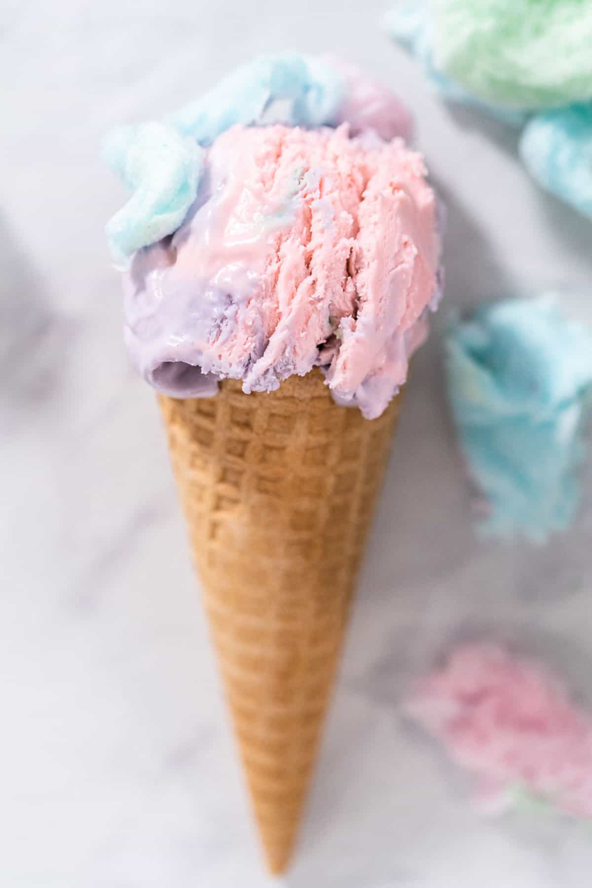 A waffle cone filled with pink and purple no churn cotton candy ice cream.