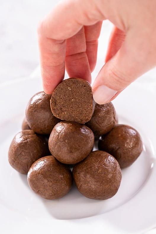 stack of protein bliss balls on white plate with hand 
