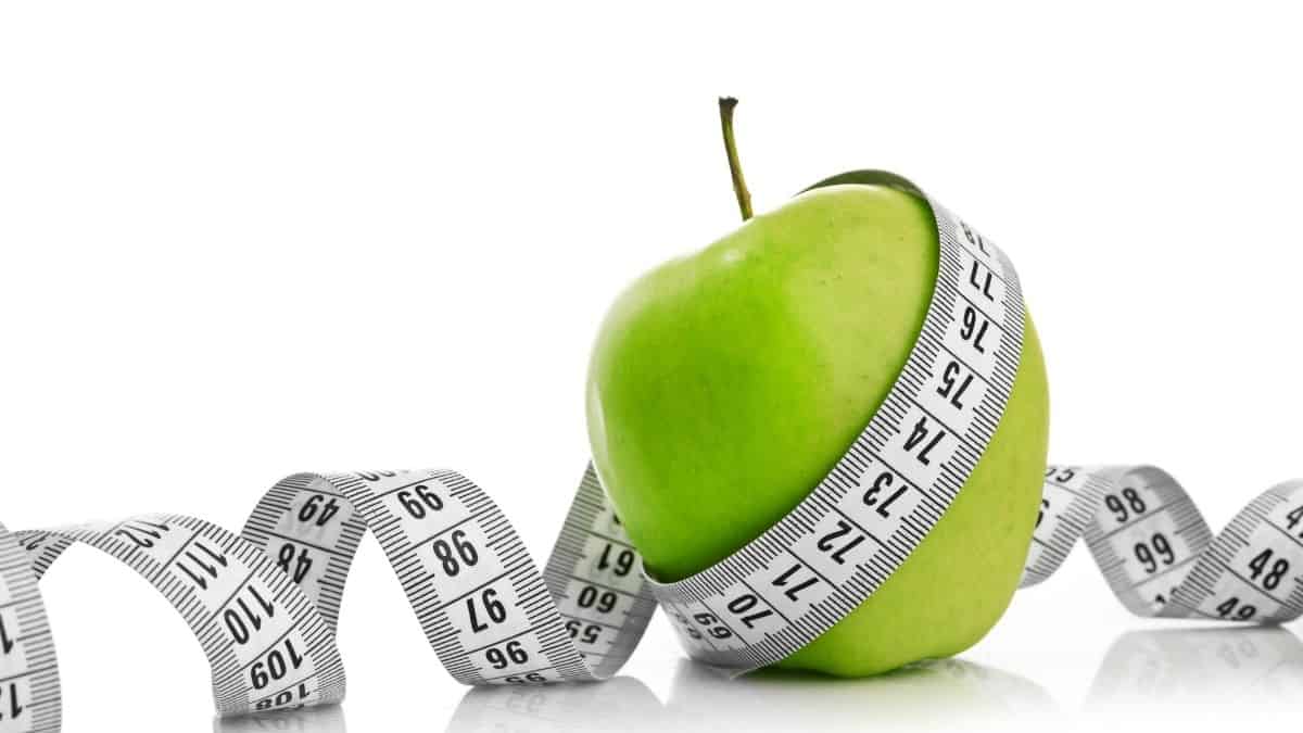 An apple wrapped with a measuring tape on a white background.