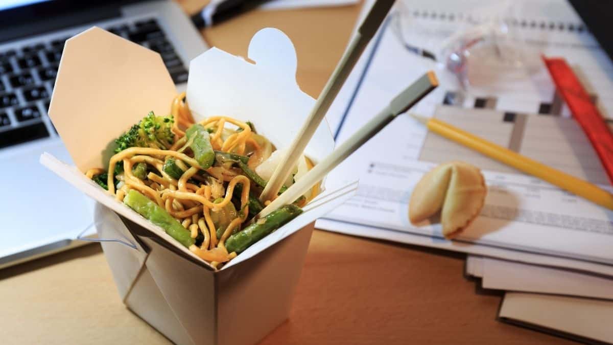 Chinese Food in a carton with chopsticks on a desk.